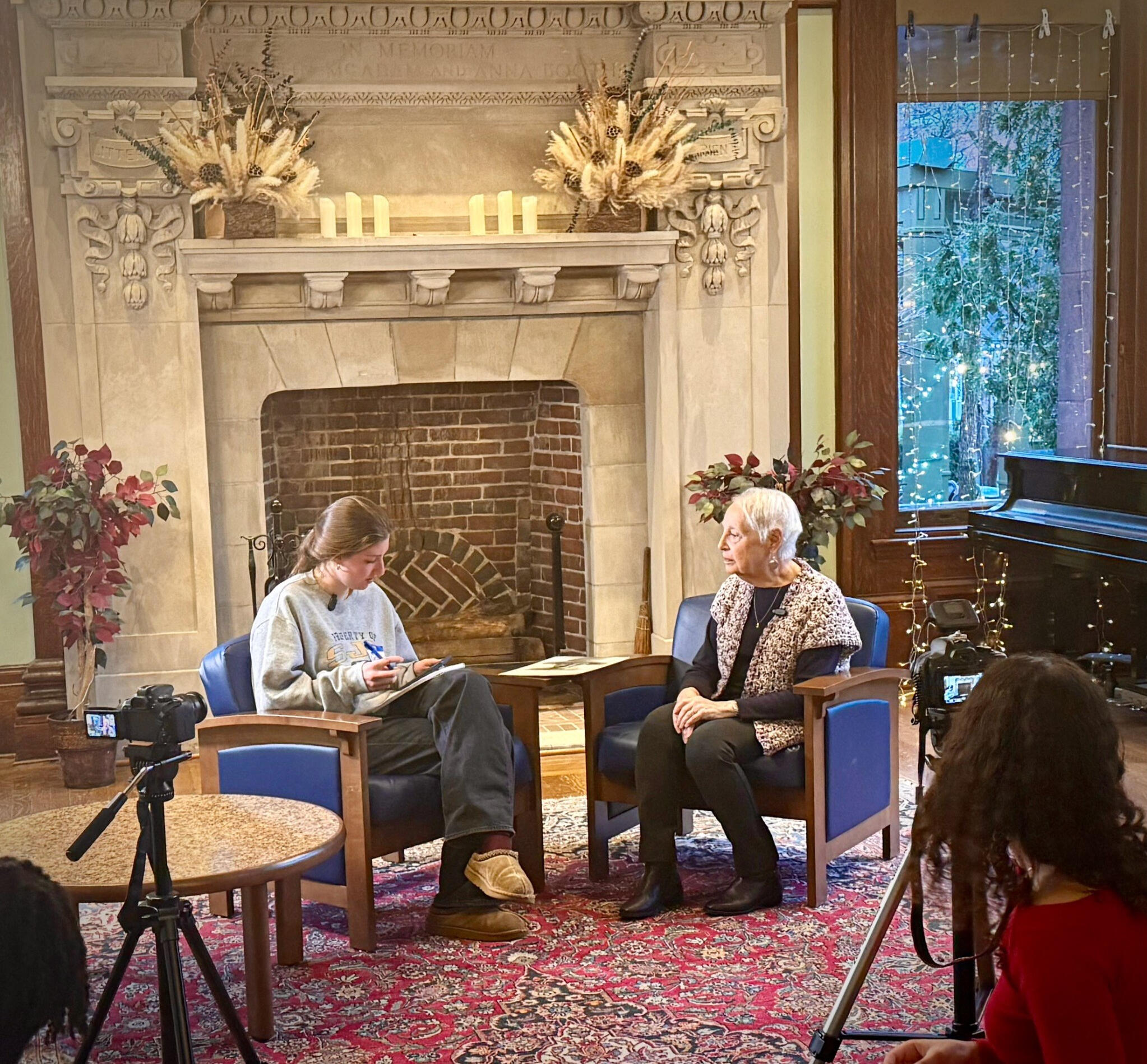 An Intergenerational Interview at Nyack Library A student filmmaker interviews a lifelong learner in front of the fireplace at Nyack Library while two cameras record their conversation.